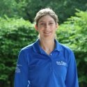 A woman in blue shirt standing next to trees.