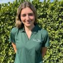 A woman in green shirt standing next to hedge.